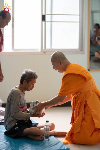 พระสงฆ์กำลังส่งมอบสิ่งของให้แก่ชายสูงวัยที่นั่งอยู่บนพื้น