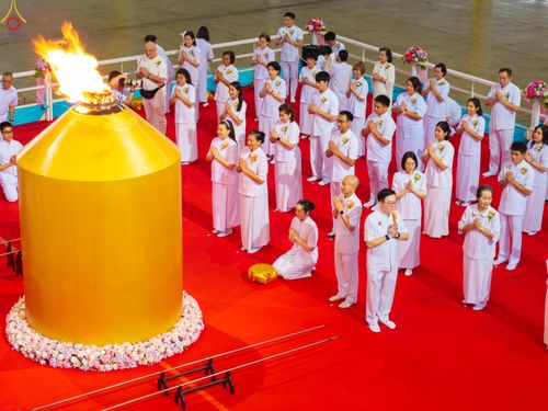กลุ่มคนในชุดขาวกำลังประกอบพิธีจุดเทียนใจ ไฟนิรันดร์ อนันตชัย โดยมีเทียนสีทองขนาดใหญ่ตั้งอยู่ด้านหน้า