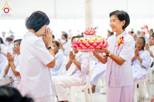หญิงชุดขาวถือพานดอกบัวสีชมพูและหญิงอีกท่านกำลังพนมมือไหว้ในพิธีทางศาสนา