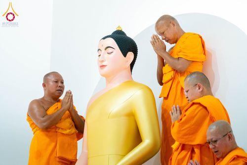 พระภิกษุสงฆ์หลายรูปกำลังพนมมือไหว้พระพุทธรูปปางสมาธิสีทองภายในอาคาร