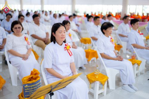 กลุ่มคนสวมชุดขาวนั่งสมาธิในพิธีทางศาสนาภายในอาคาร