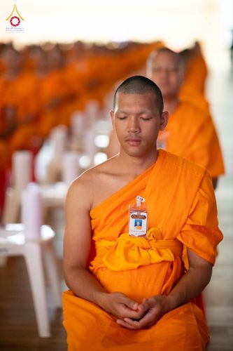 พระภิกษุสงฆ์นั่งหลับตาทำสมาธิในจีวรสีส้ม มีป้ายชื่อติดที่หน้าอก