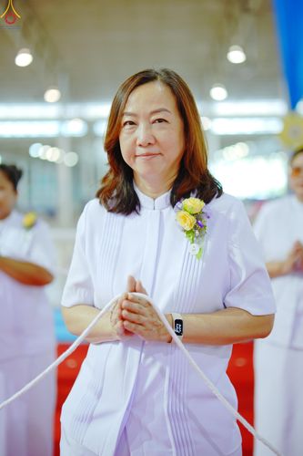 หญิงวัยกลางคนสวมชุดสีขาวถือสายสิญจน์ในพิธีจุดเทียนใจ