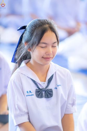 นักเรียนหญิงสวมชุดนักเรียนสีขาวผูกโบว์สีน้ำเงินกำลังหลับตาทำสมาธิด้วยท่าทางสงบ