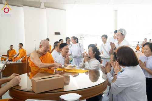 พระภิกษุสงฆ์กำลังรับถวายภัตตาหารจากพุทธศาสนิกชนที่นั่งพนมมือด้วยความเคารพ