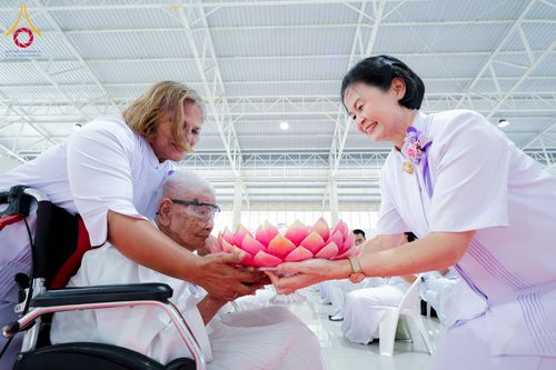 กลุ่มคนสวมชุดสีขาวกำลังประคองพานดอกบัวสีชมพูร่วมกันในพิธีทางศาสนา