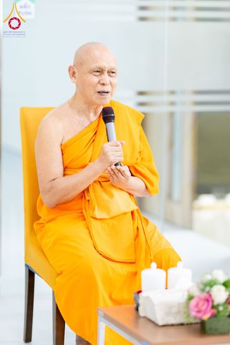 พระภิกษุสงฆ์นั่งบนเก้าอี้ถือไมโครโฟนกำลังกล่าวบรรยาย