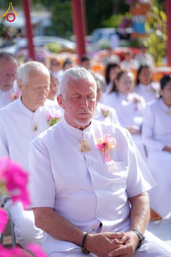 กลุ่มคนสวมชุดสีขาวนั่งหลับตาทำสมาธิในบรรยากาศพิธีทางศาสนา