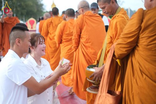 ชายหญิงคู่หนึ่งกำลังใส่บาตรพระสงฆ์ในแถวพิธีทำบุญ