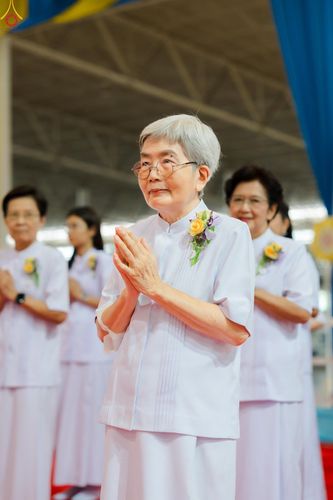 หญิงสูงวัยสวมชุดสีขาวพนมมือด้วยท่าทางสงบในพิธีทางศาสนา