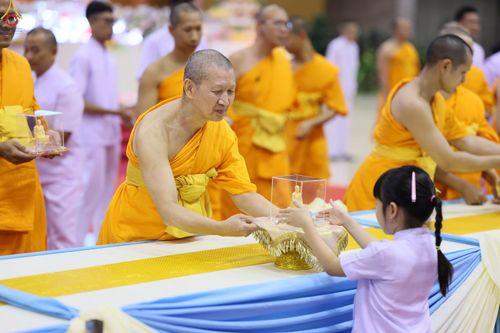 พระภิกษุกำลังส่งมอบพระของขวัญในกล่องใสให้แก่เด็กหญิงในพิธีการ