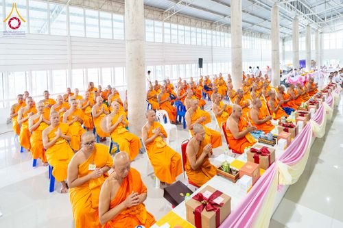 พระภิกษุสงฆ์จำนวนมากนั่งพนมมือร่วมพิธีทางศาสนาภายในอาคารโถงกว้าง