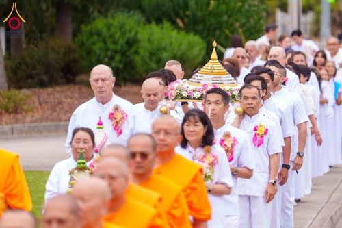 กลุ่มคนสวมชุดขาวและพระภิกษุสงฆ์เดินในขบวนอัญเชิญบุษบกประดิษฐานพระบรมสารีริกธาตุ