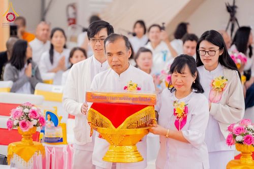 กลุ่มคนสวมชุดขาวกำลังถือพานพุ่มที่มีผ้าไตรในพิธีทอดผ้าป่า