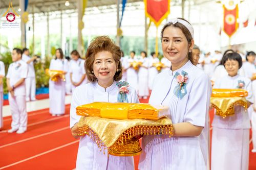 หญิงสองท่านสวมชุดสีขาวถือพานผ้าไตรสีเหลืองทองในพิธีทางศาสนา