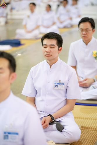 ชายสวมชุดขาวนั่งสมาธิหลับตาอย่างสงบร่วมกับกลุ่มคนในสถานที่ปฏิบัติธรรม