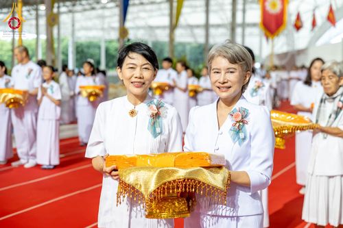 หญิงไทยสองท่านสวมชุดสีขาวถือพานผ้าไตรจีวรในพิธีทางศาสนา