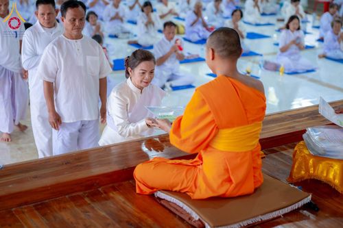 พระภิกษุสงฆ์ในจีวรสีส้มกำลังมอบเกียรติบัตรให้แก่สุภาพสตรีที่สวมชุดสีขาวในพิธีอบรม