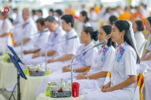 กลุ่มคนสวมชุดสีขาวนั่งเรียงแถวในพิธีทางศาสนา มีไมโครโฟนตั้งอยู่ด้านหน้า