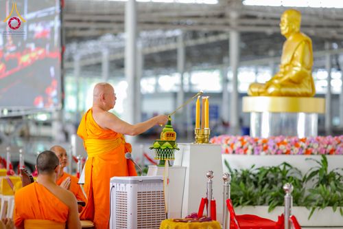 พระภิกษุสงฆ์ในจีวรสีส้มกำลังจุดเทียนบูชาหน้าพระพุทธรูปทองคำในอาคารขนาดใหญ่