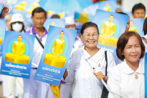 กลุ่มคนสวมชุดสีขาวถือป้ายภาพองค์พระประธานในขบวนแห่