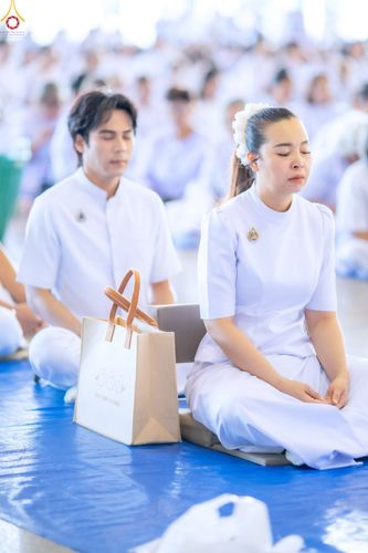 ชายและหญิงสวมชุดขาวนั่งสมาธิในพิธีตักบาตร