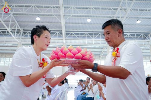 ชายและหญิงสวมชุดสีขาวกำลังประคองพานดอกบัวสีชมพูร่วมกันในพิธีกรรมทางศาสนา