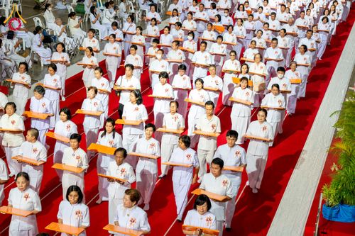 กลุ่มพุทธศาสนิกชนสวมชุดขาวถือพานผ้าป่าเดินแถวบนพรมแดงในพิธีทางศาสนา