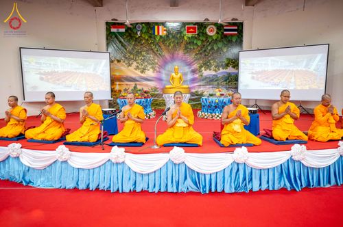 คณะสงฆ์จำนวนหลายรูปนั่งพนมมือเรียงแถวบนเวทีที่มีฉากหลังเป็นภาพพระพุทธรูปและธงชาติหลายประเทศ