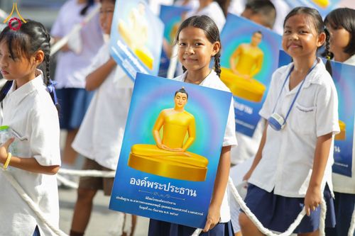 นักเรียนหญิงยิ้มแย้มถือป้ายรูปองค์พระประธานสีทองในกิจกรรมทางศาสนา