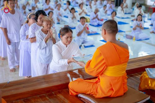 อุบาสิกาแก้วสวมชุดขาวกำลังรับมอบเกียรติบัตรจากพระภิกษุสงฆ์ในพิธีอบรม