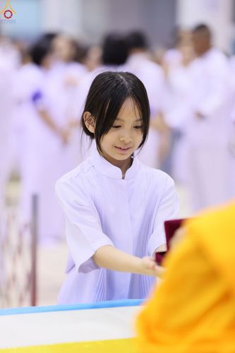 เด็กหญิงสวมชุดสีขาวกำลังรับกล่องพระของขวัญจากพระภิกษุด้วยความตั้งใจ
