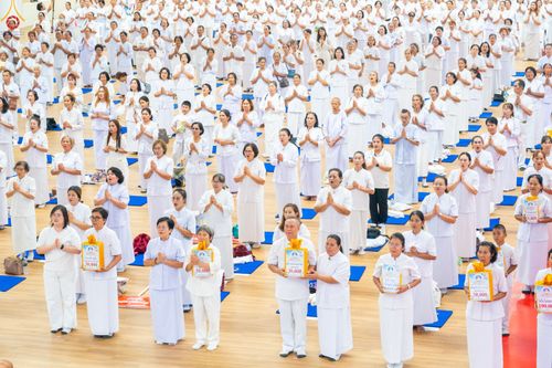 กลุ่มพุทธศาสนิกชนสวมชุดขาวจำนวนมากยืนเรียงแถวร่วมกิจกรรมทางศาสนาภายในอาคาร