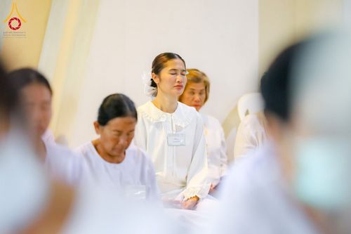 กลุ่มผู้หญิงสวมชุดสีขาวนั่งหลับตาทำสมาธิในห้องปฏิบัติธรรม