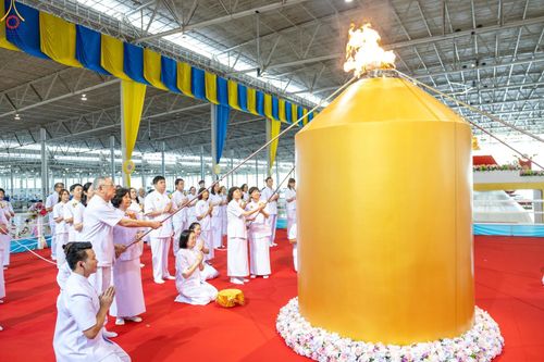 กลุ่มคนในชุดสีขาวกำลังร่วมพิธีจุดไฟบนแท่นสีทองขนาดใหญ่ภายในอาคาร