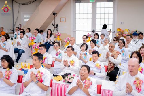 กลุ่มคนสวมชุดสีขาวนั่งพนมมือร่วมพิธีทางศาสนาภายในอาคาร