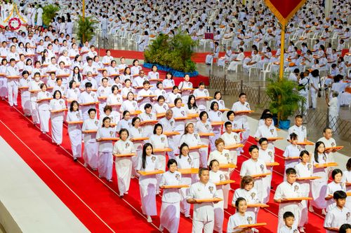 กลุ่มพุทธศาสนิกชนสวมชุดขาวถือพานผ้าป่าเดินแถวบนพรมสีแดงในพิธีทางศาสนา ณ สภาธรรมกายสากล