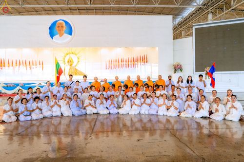 กลุ่มพระภิกษุและพุทธศาสนิกชนชุดขาวถ่ายภาพร่วมกันภายในอาคารสภาธรรมกายสากล