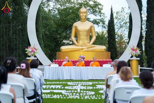 พระภิกษุสงฆ์ 3 รูปนั่งหน้าพระพุทธรูปทองคำและกลุ่มสาธุชนที่มาร่วมกิจกรรมนั่งสมาธิและจุดประทีป