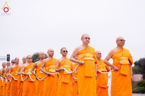 คณะสงฆ์หลายรูปในจีวรสีส้มเดินแถวถือสายสิญจน์ในพิธีทางศาสนา