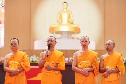 พระภิกษุสงฆ์ 4 รูปยืนเรียงแถวหน้าพระพุทธรูป โดยรูปที่สองจากซ้ายกำลังถือไมโครโฟนพูด