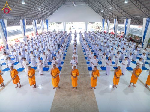 กลุ่มผู้เข้าร่วมโครงการในชุดขาวและพระภิกษุสงฆ์ยืนเรียงแถวภายในอาคารปฏิบัติธรรม