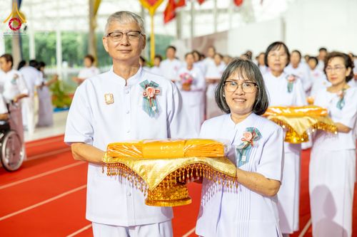 ชายและหญิงสวมชุดขาวถือพานผ้าไตรจีวรในพิธีทอดผ้าป่า