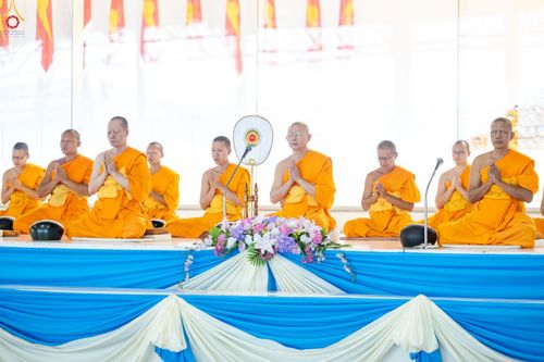 พระสงฆ์หลายรูปนั่งพนมมือบนเวทีที่มีการตกแต่งด้วยผ้าสีฟ้าและสีขาวในพิธีทางศาสนา