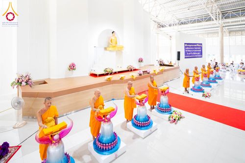 พระภิกษุสงฆ์ในจีวรสีส้มกำลังประกอบพิธีทางศาสนาหน้าเกศดอกบัวตูมจำลองภายในอาคาร