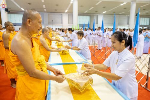 พระภิกษุสงฆ์และอุบาสิกาสวมชุดขาวกำลังประกอบพิธีมอบพระของขวัญภายในห้องโถง