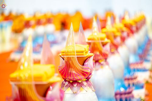 พานพุ่มสีชมพูทองวางเรียงรายพร้อมผ้าไตรสีเหลืองทองในพิธีทางศาสนา