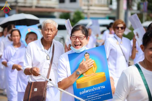 กลุ่มคนสวมชุดขาวถือป้ายภาพพระประธานเดินในขบวนกลางแจ้ง