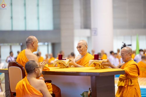 พระภิกษุสงฆ์ในจีวรสีส้มกำลังทำพิธีมอบพระของขวัญบนโต๊ะที่มีผ้าคลุมสีเหลือง