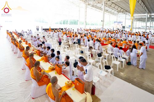 พระภิกษุและสาธุชนจำนวนมากนั่งเรียงรายตามโต๊ะยาวภายในอาคารขนาดใหญ่เพื่อร่วมพิธีถวายสังฆทาน